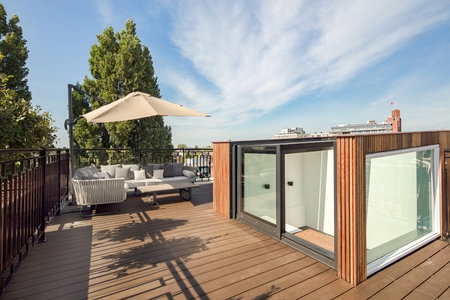 a roof deck with an umbrella and patio furniture set up on the deck, under a blue sky filled with white cloudsのeditorial素材