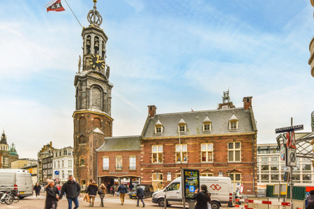 Amsterdam, Netherlands - 10 April, 2021: some people walking around in front of a building with a clock on its face and the sky is blueのeditorial素材