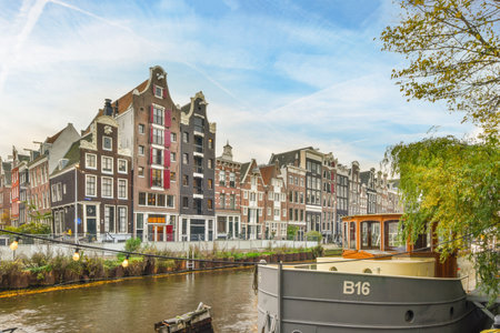 Amsterdam, Netherlands - 10 April, 2021: some boats in the water and buildings on the other side of the river, with blue sky above them all aroundのeditorial素材