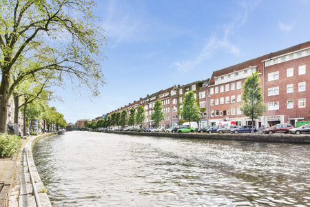 Amsterdam, Netherlands - 10 April, 2021: some buildings on the side of a body of water with cars parked along it and trees in the foresのeditorial素材