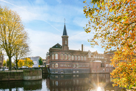 an old brick building on the side of a river with autumn leaves in front and blue sky over water belowのeditorial素材