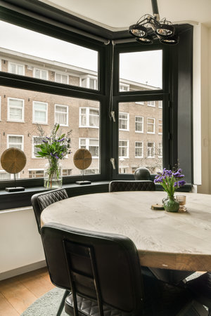 a dining table and chairs in front of a large window looking out at the city outside with flowers on itの写真素材