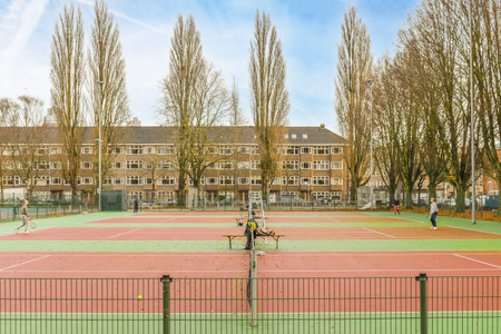 an outdoor tennis court with trees in the background and two people playing tennis on the other side of the courtのeditorial素材