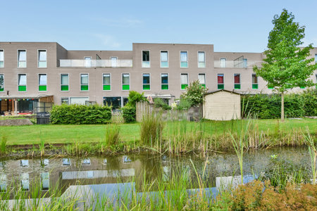 Amsterdam, Netherlands - 10 April, 2021: an apartment complex with water and trees in the foregrounds, near to where there is a small pondのeditorial素材
