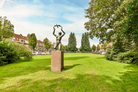 Amsterdam, Netherlands - 10 April, 2021: a statue in the middle of a green lawn with trees and houses in the background on a bright sunny dayのeditorial素材