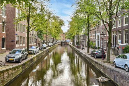 a canal with cars parked on the side and trees lining the street in front of the house, along itのeditorial素材