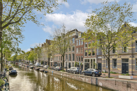 Amsterdam, Netherlands - 10 April, 2021: a canal in the middle of an urban area with cars parked on both sides and trees growing along the sideのeditorial素材