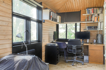 a bedroom with a bed, desk and books on the wall behind it is a window that looks out onto treesのeditorial素材