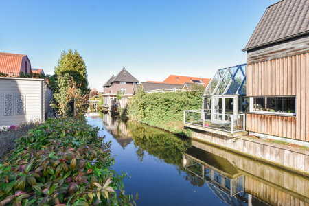 Amsterdam, Netherlands - 10 April, 2021: a canal with houses on the other side and trees in the foregrounds along the waters edgeのeditorial素材