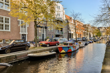 some boats parked on the side of a canal with buildings in the background and trees growing along the waters edgeのeditorial素材