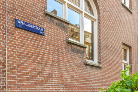 a street sign on the side of a brick building with green plants growing in front of it and a windowのeditorial素材