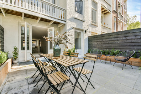 a patio with wooden tables and chairs in front of an apartment building that has white brick walls on both sidesのeditorial素材