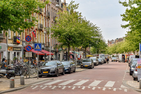 Amsterdam, Netherlands - 10 April, 2021: a city street with cars parked on both sides and people walking down the sidewalk in the distance is an intersectionのeditorial素材