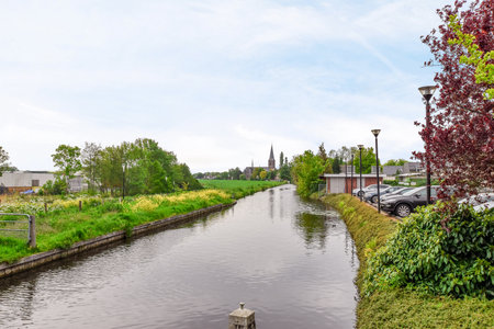 Amsterdam, Netherlands - 10 April, 2021: a canal with cars parked on the side and houses in the distance, along its banked waterwayのeditorial素材