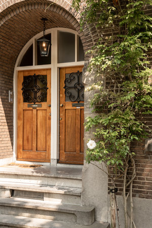 two wooden doors in front of a brick building with green leaves growing on the door and steps leading up to itのeditorial素材