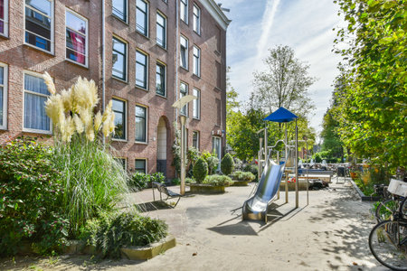 Amsterdam, Netherlands - 10 April, 2021: a playground in the middle of an apartment complex, with lots of plants and trees on either side of the buildingのeditorial素材