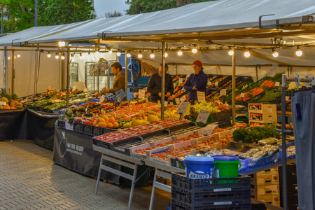 an outdoor market with fruits and vegetables for sale in the evening light, on a brick paved street lined with peopleのeditorial素材
