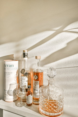 Amsterdam, Netherlands - 10 April, 2021: some bottles and glasses on a white shelf in a room with light coming through the window onto the wall behind itのeditorial素材