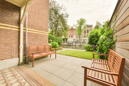 an outside area with wooden benches and plants on the side walk way, in front of a bricked building