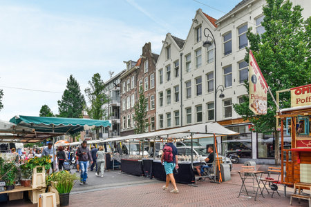 Amsterdam, Netherlands - 10 April, 2021: an outdoor market area with people walking around and vendors selling food on the sidewalk in front of a large white buildingのeditorial素材