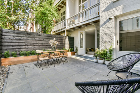 a patio with chairs, tables and plants on the side walk way in front of a white brick apartment buildingのeditorial素材