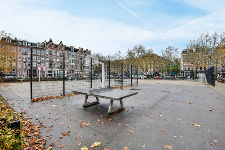 a bench in the middle of an empty street with leaves on the ground and buildings in the distance behind itのeditorial素材
