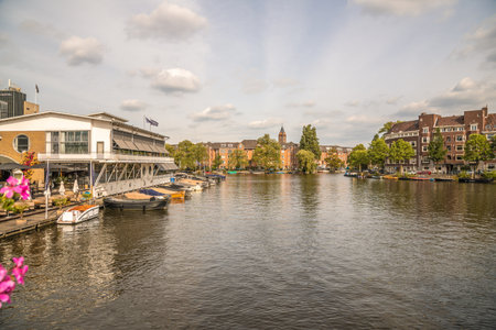 a river with boats in the water and buildings on both sides, as seen from across the canal there is a cloudy blue skyのeditorial素材