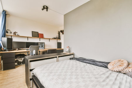 Amsterdam, Netherlands - 10 April, 2021: a bedroom with a bed, desk and computer monitor on the wall in front of the rooms windowsのeditorial素材