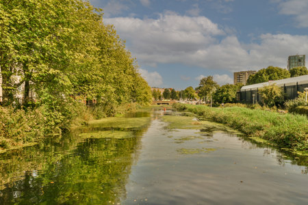 Amsterdam, Netherlands - 10 April, 2021: a river in the middle of an urban area with buildings and trees on both sides there is a cloudy blue skyのeditorial素材