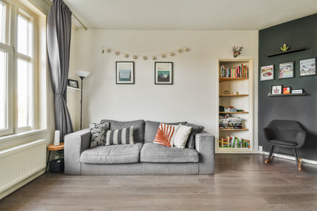 a living room with a grey couch and books on the shelves in front of the sofa is a bookcaseのeditorial素材