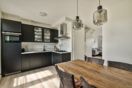 a kitchen and dining area in a house with wood flooring, white walls, black cabinets and stainless appliancesのeditorial素材