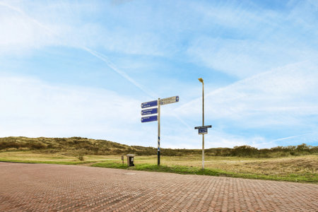 a street sign in front of a blue sky with white clouds and some green grass on the other side of the roadのeditorial素材