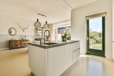 Amsterdam, Netherlands - 10 April, 2021: a modern kitchen with white cabinets and black counter tops in an open living room looking out to the garden outsideのeditorial素材