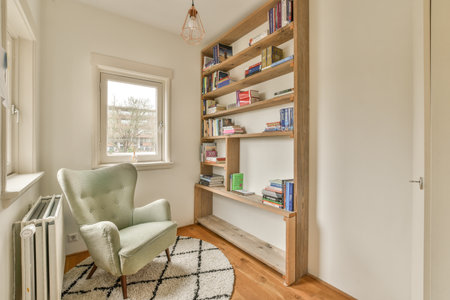 a room with a chair, bookshels and a book shelf on the wall next to an open windowのeditorial素材