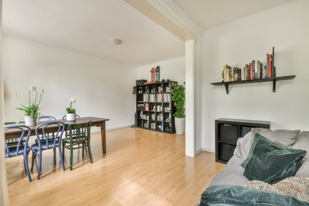 a living room with wood flooring and white walls, there is a small dining table in front of the couchのeditorial素材
