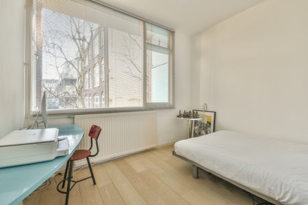 a bedroom with a bed, desk and computer on the table in front of the window looking out onto the...