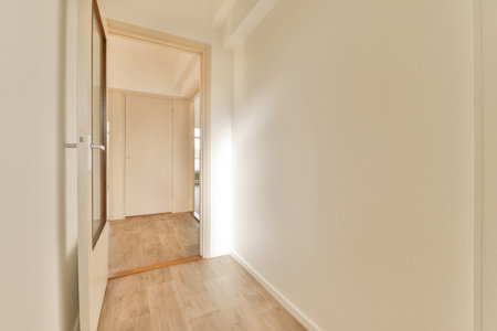 an empty room with wood flooring and white walls on the right side of the room, there is a door leading to anotherの写真素材