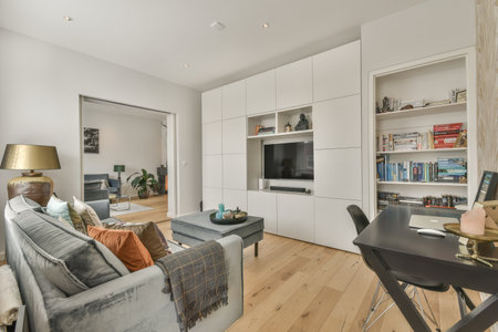 a living room with wood flooring and white cabinetd walls, including a grey couch in the middle part of the roomのeditorial素材