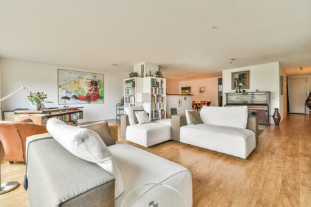 a living room with wood flooring and white couches in the center of the room is a large painting on the wallのeditorial素材