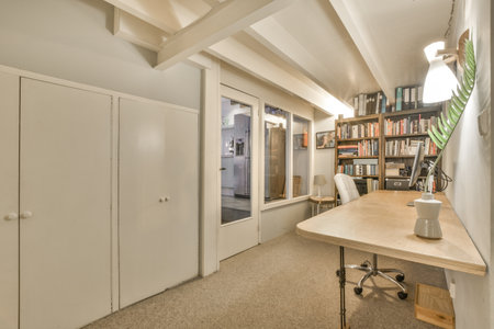 a room with a desk, bookshels and an open door that leads to the living area on the other side