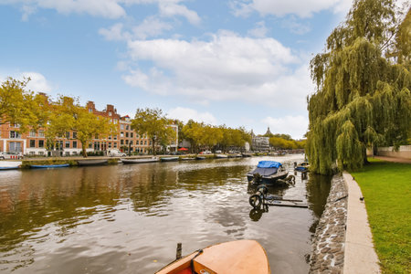 Amsterdam, Netherlands - 10 April, 2021: some boats on the water and buildings in the background, with trees lining the riverbanks to the rightのeditorial素材