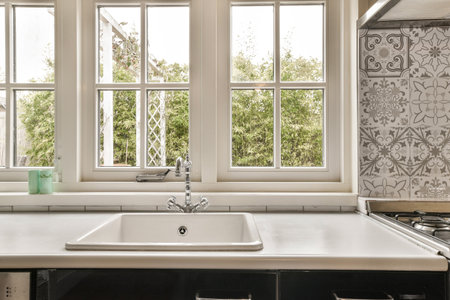 a kitchen sink in front of two windows with flowers on the wall behind it and a window to the...