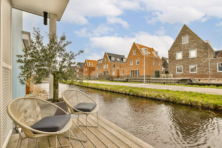an outside area with chairs and tables on the side of a river in front of a row of brick houses