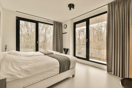 a bedroom with a bed and large windows looking out onto the trees that line the side of the room,の写真素材
