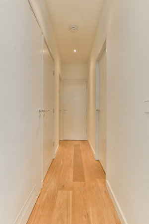 a long hallway with white walls and wood flooring on either side by side, leading to the other rooms