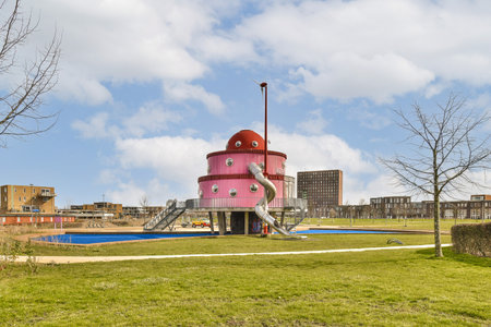 a pink house in the middle of a green field with trees and buildings in the background on a cloudy dayの写真素材