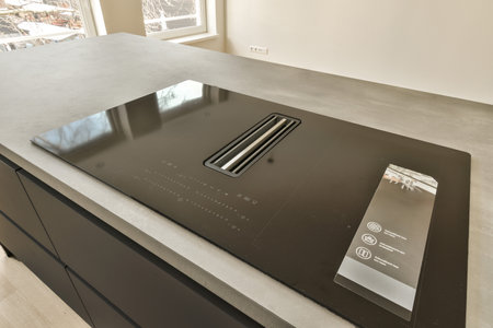 a black stove top on a kitchen counter with an oven in the background and a window to the right sideの写真素材