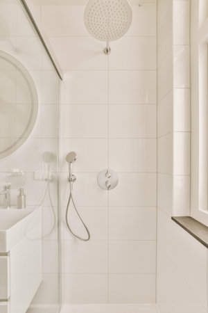 a white bathroom with a shower head and hand held in front of the mirror above it is an image of a large round mirrorの写真素材