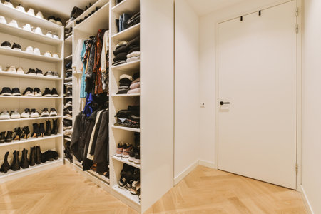 a walk - in closet with lots of shoes on the shelfs and clothes hanging on the wall behind itの写真素材