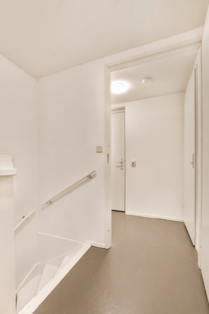 an empty room with white walls and grey flooring on the right, there is a door leading to another...